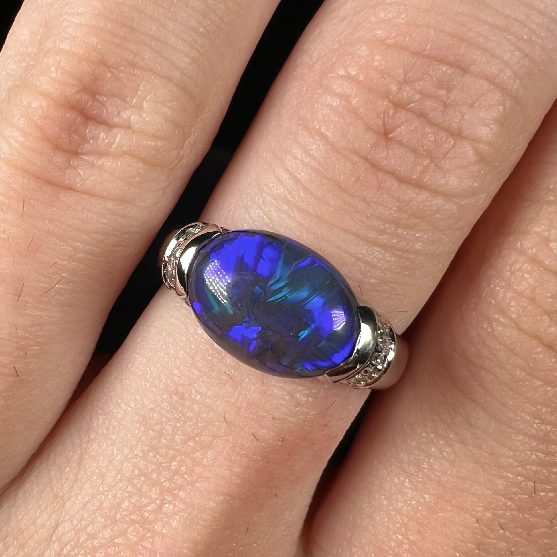 An oval cut Lightning Ridge black opal set East-West in a platinum ring with diamond accents.