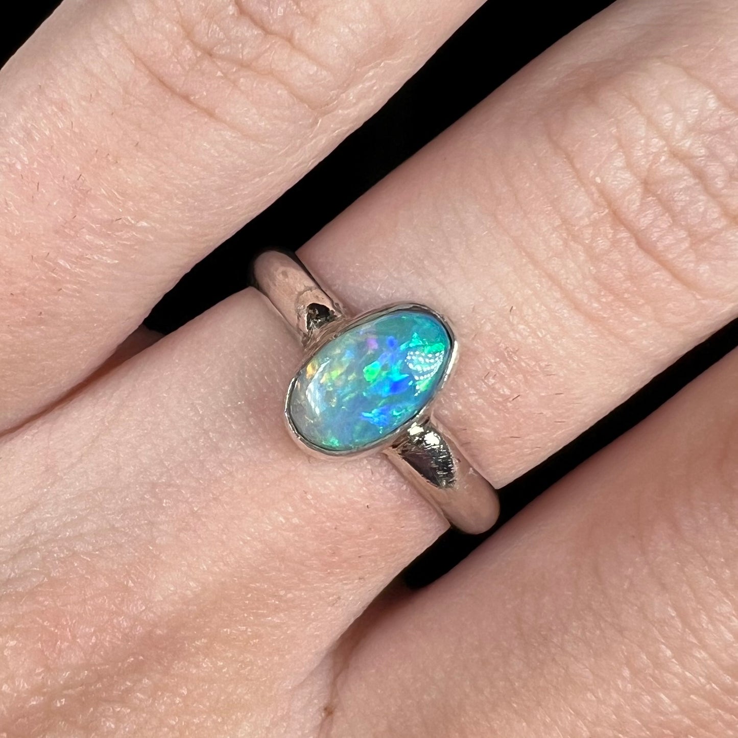 Close-up of a Lightning Ridge semi-crystal opal solitaire ring in sterling silver, worn on a finger in cool LED studio light.