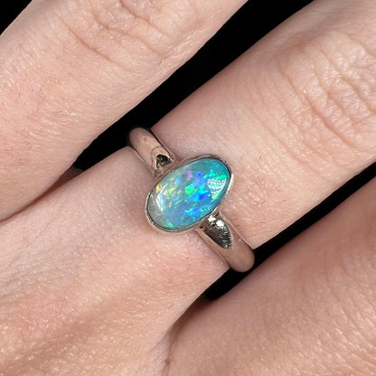 Close-up of a Lightning Ridge semi-crystal opal solitaire ring in sterling silver, worn on a finger in cool LED studio light.