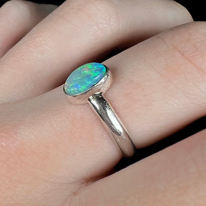 Angled close-up of a Lightning Ridge light semi-crystal opal ring made from sterling silver, worn on a finger under cool LED light.