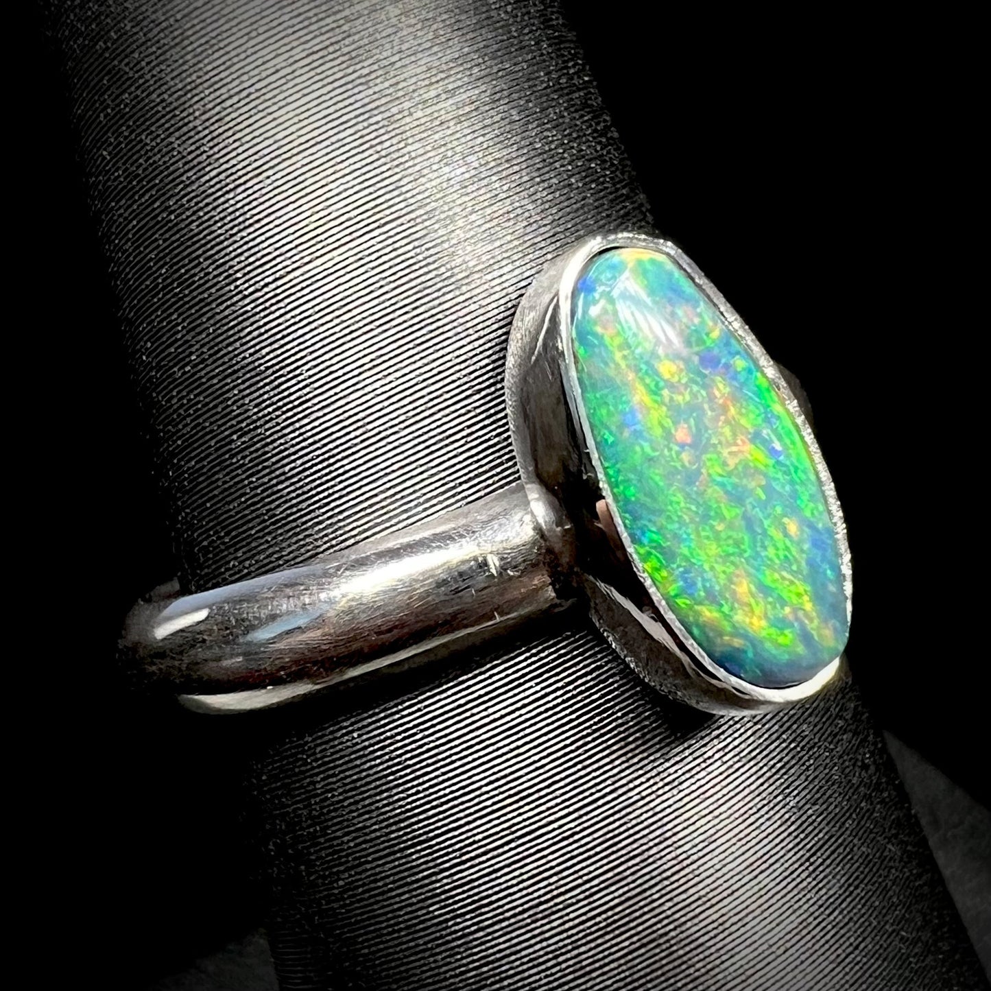 Angled close-up of an N5 dark Lightning Ridge opal solitaire ring made from sterling silvere, shown on a ring display.  The opal has green fire.