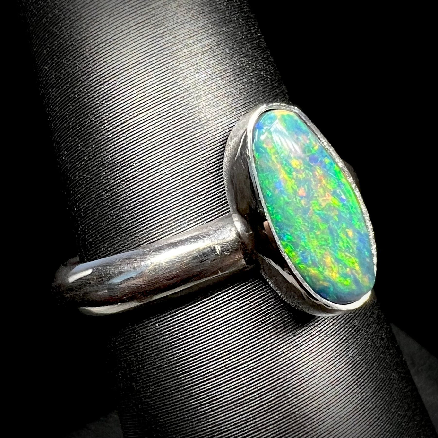 Angled close-up of an N5 dark Lightning Ridge opal solitaire ring made from sterling silvere, shown on a ring display.  The opal has green fire.