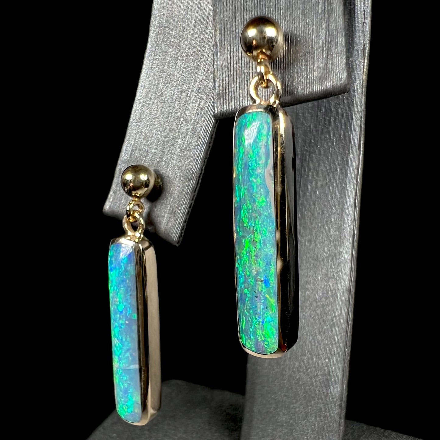 A pair of Lightning Ridge opal drop earrings set in yellow gold, shown at an angle.