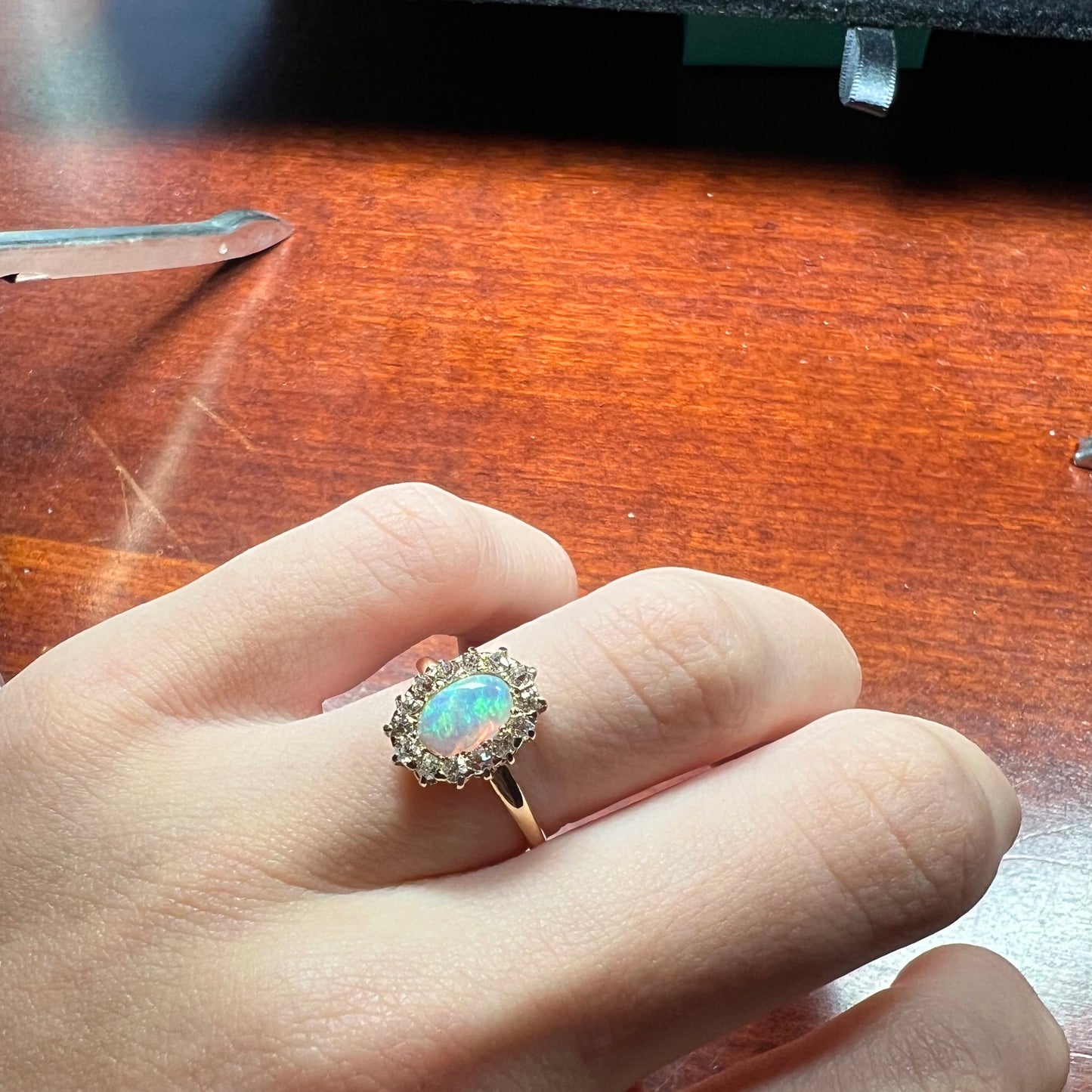 An opal and diamond halo engagement ring on a hand.  The opal shines green and blue colors.