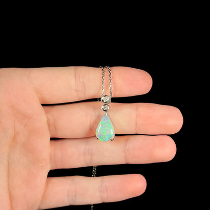 A platinum drop pendant mounted with two diamond accents and a pear shaped green-blue crystal opal.