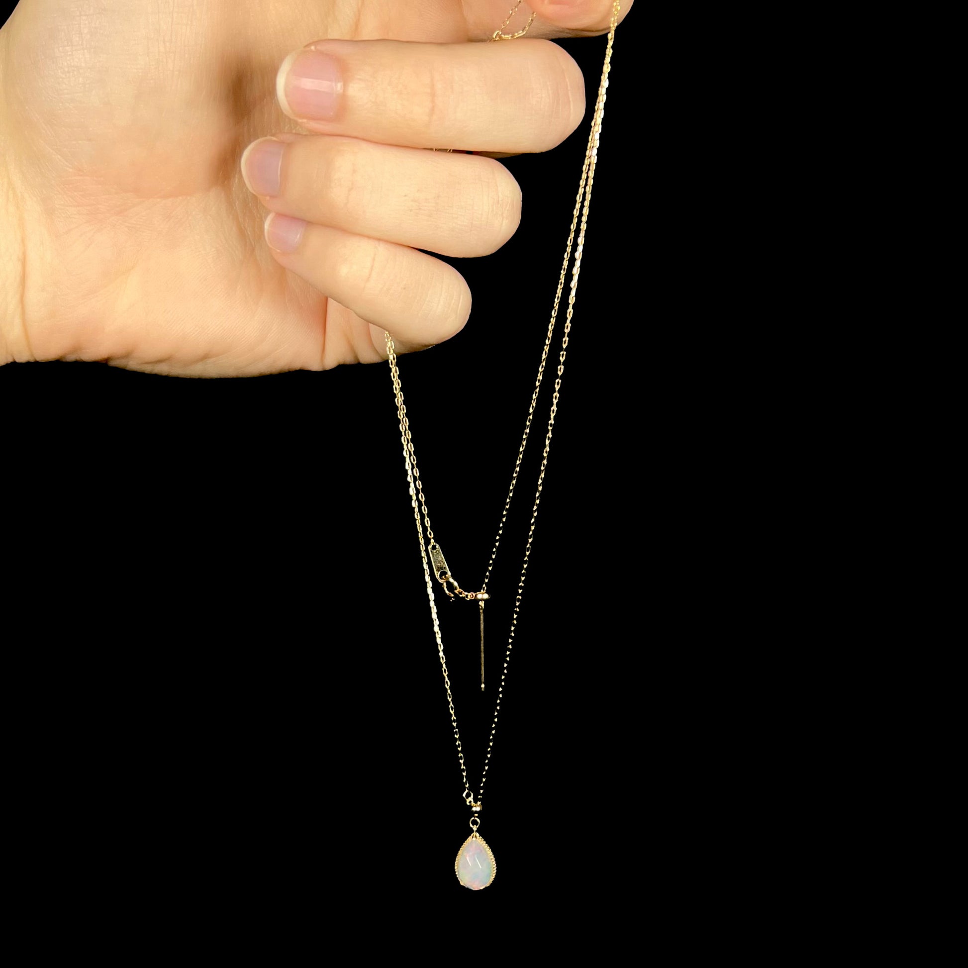 Long adjustable opal necklace dangling in a hand against a black background. The chain is noticeably long in proportion to the opal.