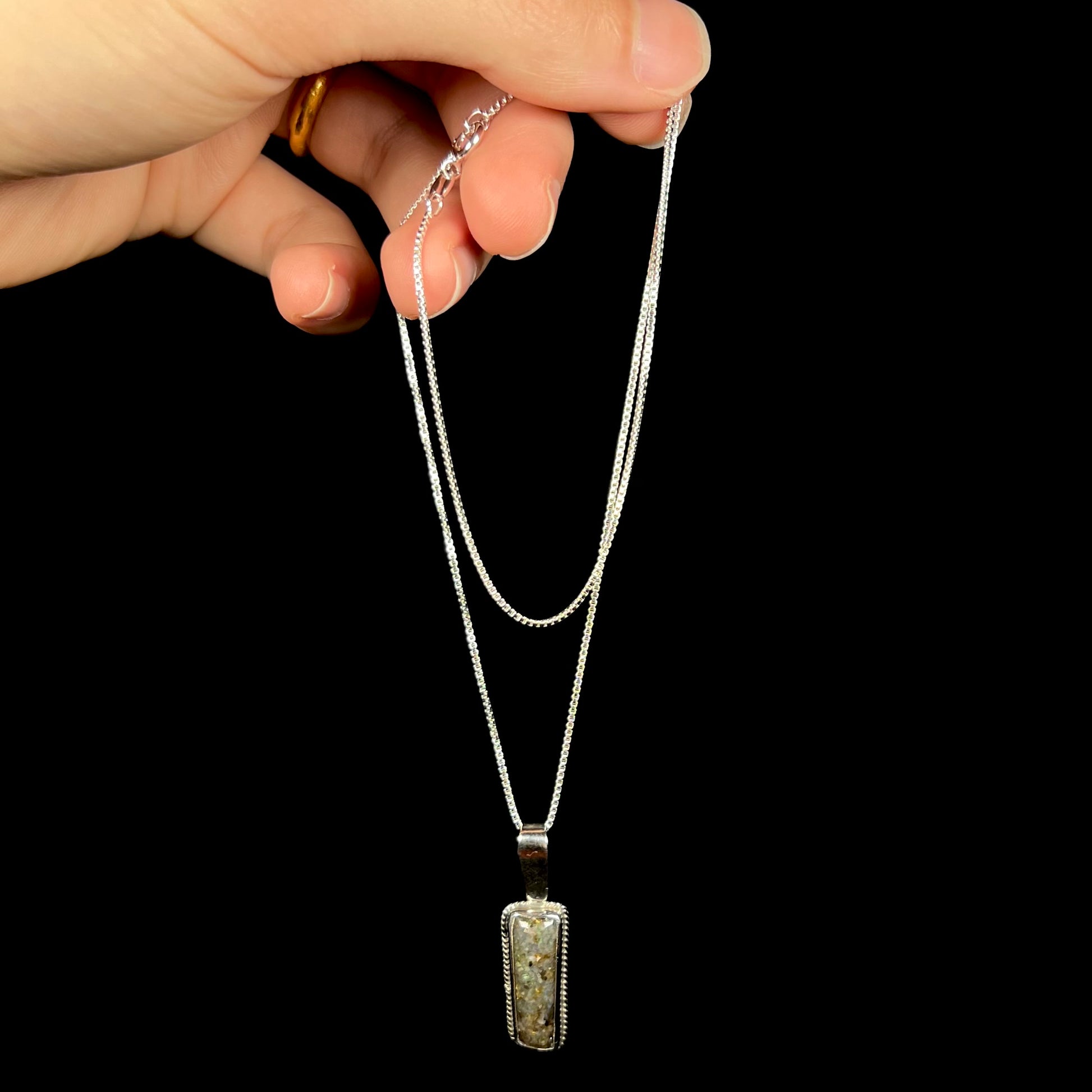 A Louisiana matrix opal necklace in sterling silver, dangled from its chain by a hand against a black background.