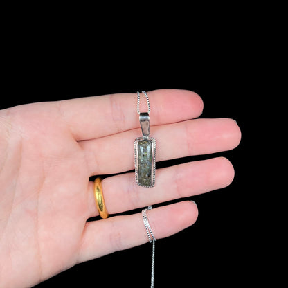 A Louisiana matrix opal necklace in sterling silver shown in a hand against a black background.