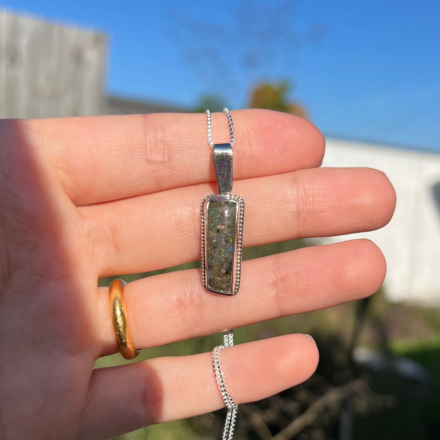 A Louisiana matrix opal pendant in sterling silver shown in a hand in the sunlight.