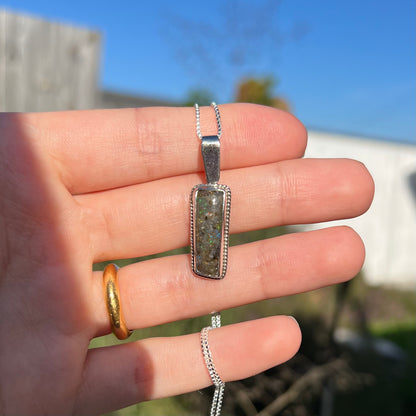 A Louisiana matrix opal pendant in sterling silver shown in a hand in the sunlight.