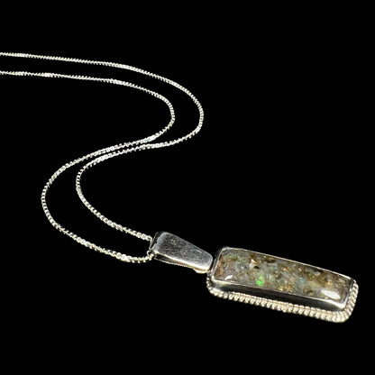 A Louisiana matrix opal necklace in sterling silver, shown from an angle laying against a black background.