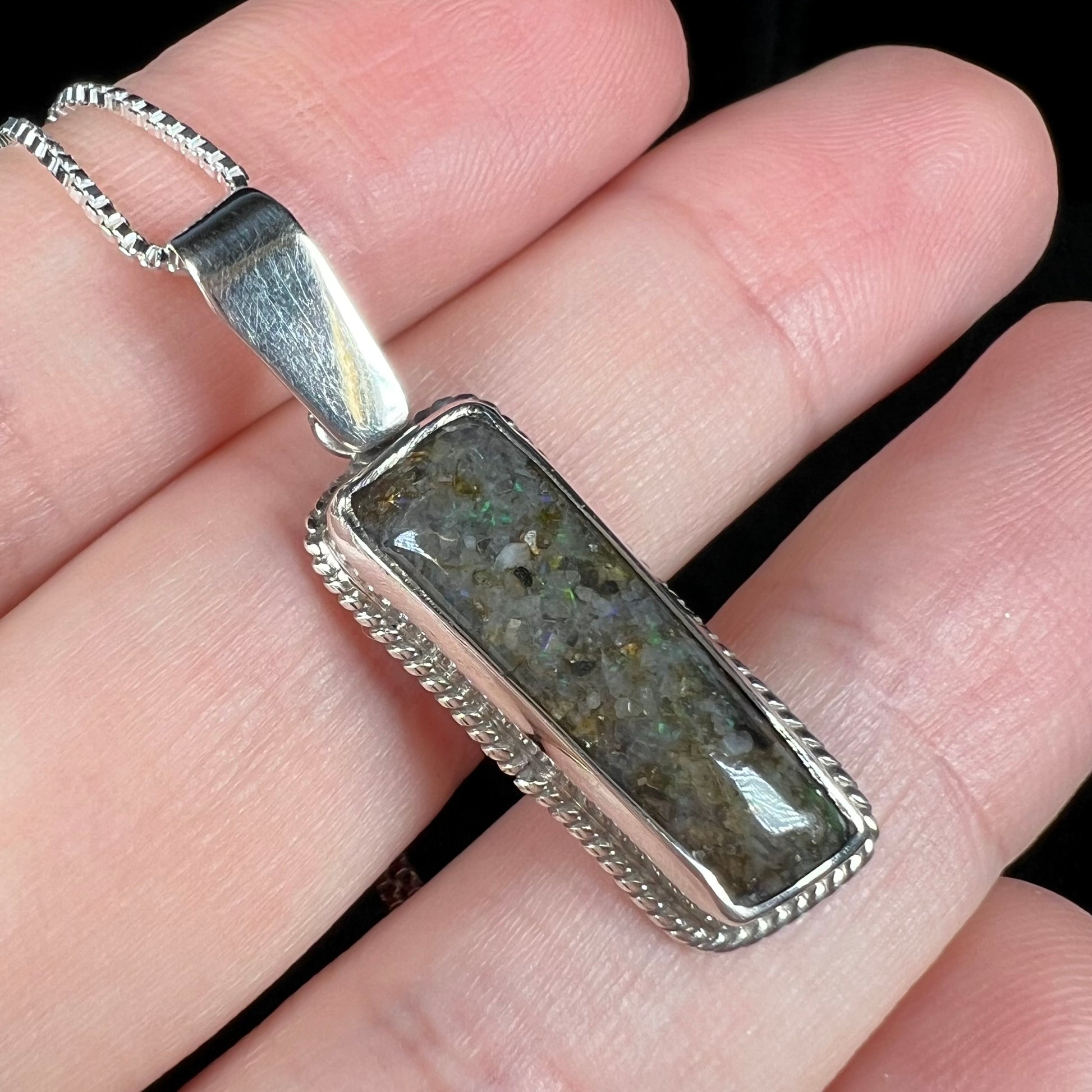 A Louisiana matrix opal pendant in sterling silver shown close-up from an angle in a hand.