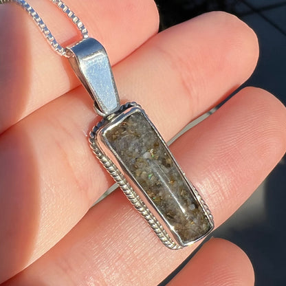 A Louisiana matrix opal pendant in sterling silver shown close-up from an angle in the sunlight, held in a hand.