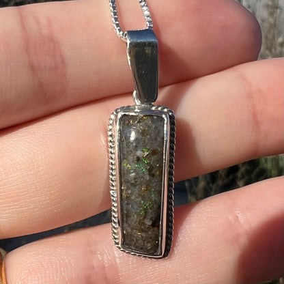A Louisiana matrix opal pendant in sterling silver shown close-up in the sunlight, held in a hand.