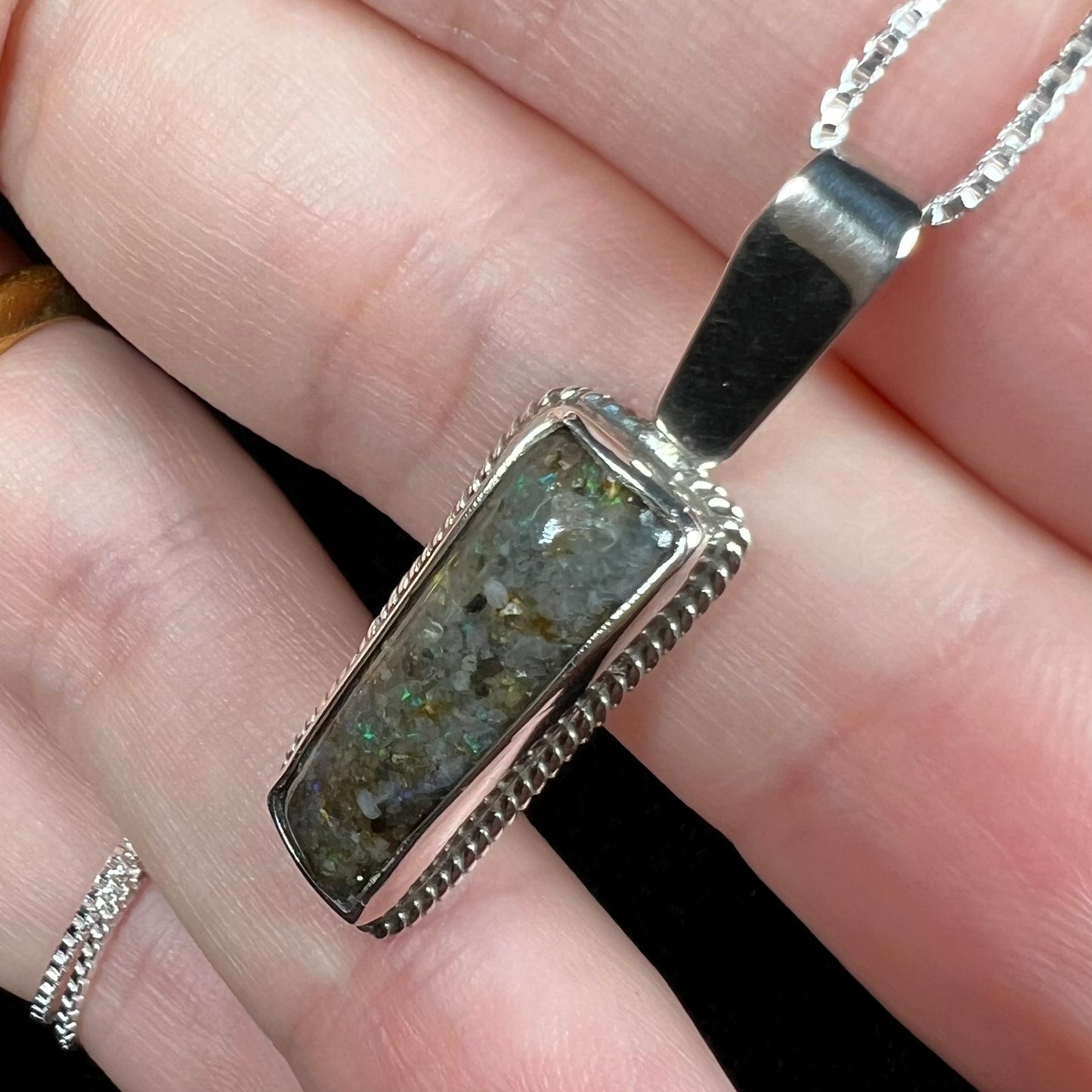 Close-up angled view of a Louisiana matrix opal pendant in sterling silver, shown in a hand.