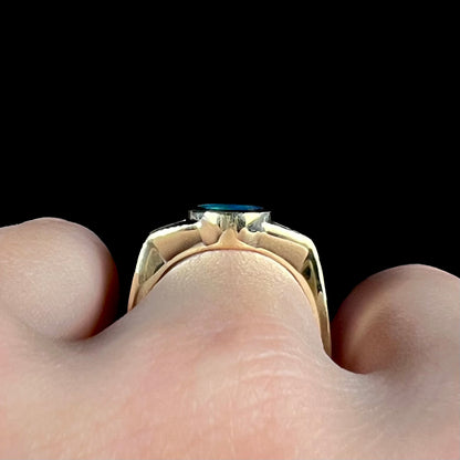 Side gallery view of a low-profile opal ring in 18k yellow gold, worn on a finger against a black background.