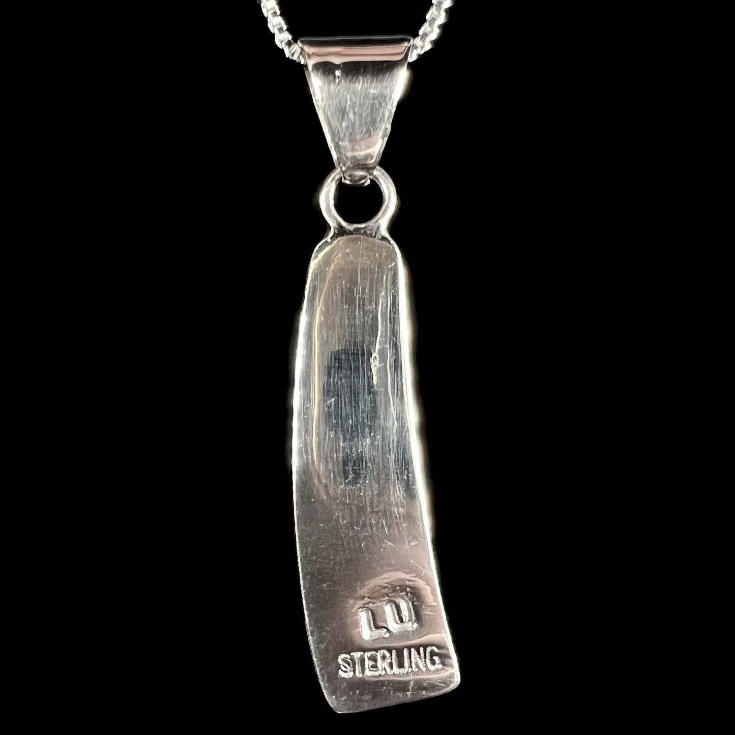 Back side of sterling silver pendant stamped "LU STERLING", shown on black background.