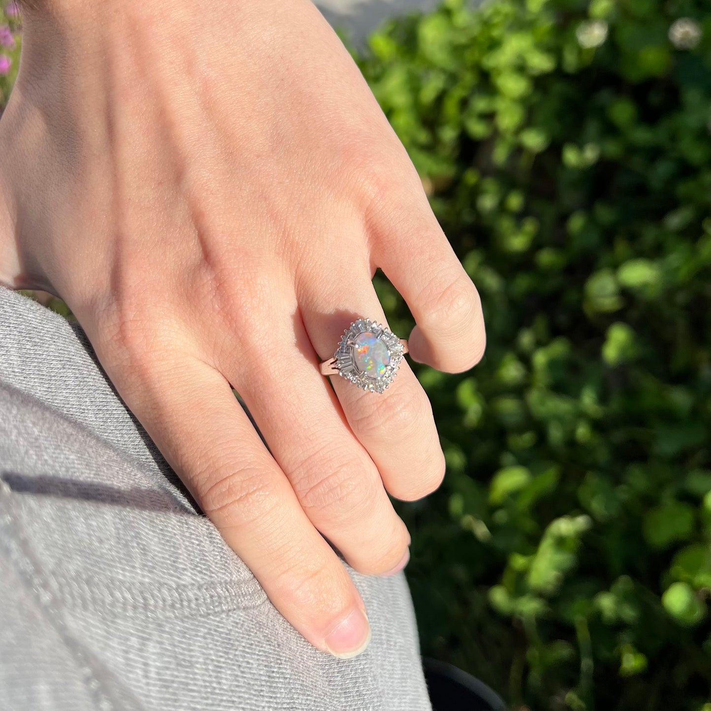 Vintage opal and diamond ring worn on a hand, captured in natural daylight, showcasing its elegant platinum setting and red-blue opal fire.