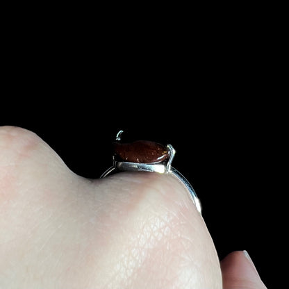 Macro gallery view of the fire agate ring worn on hand with black background.