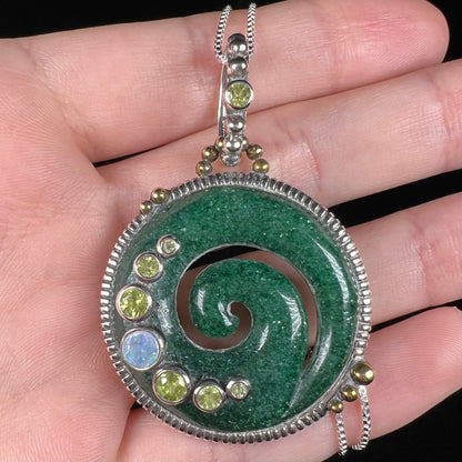 A men's aventurine koru necklace, accented with opal and peridot, shown close-up in a hand.