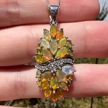 Close-up of a sterling silver Ethiopian opal pendant, resting on fingers in sunlight.  Marquise cut and round cut fire opals form a clustered design.