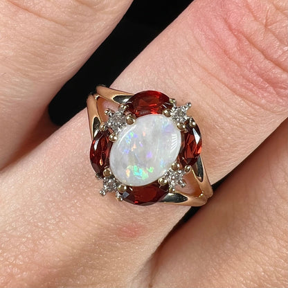 A ladies natural opal ring in yellow gold.  The opal is surrounded by red marquise cut garnets and diamonds.