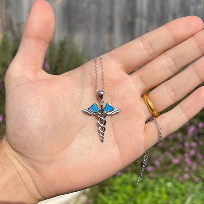A silver plated medical caduceus pendant with blue lab-created opal inlay.