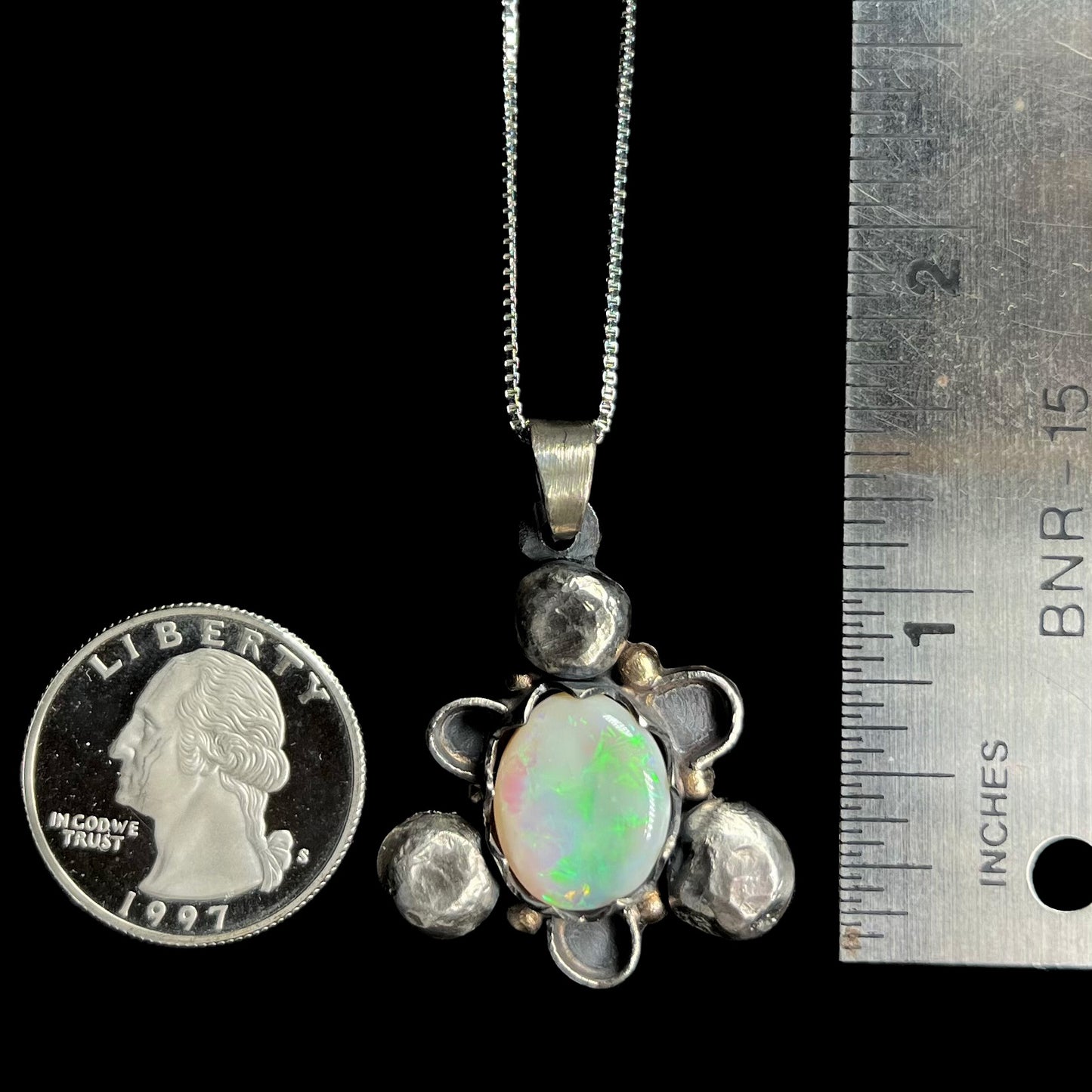 A 1.5 inch long men's rustic two-tone sterling silver and gold Australian opal pendant next to a quarter and ruler.