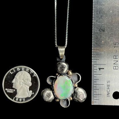 A 1.5 inch long men's rustic two-tone sterling silver and gold Australian opal pendant next to a quarter and ruler.