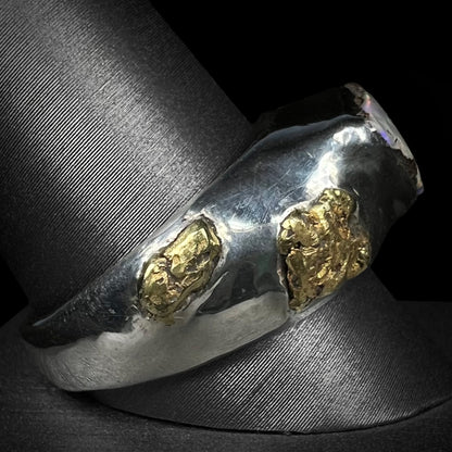 Side profile view of a men's sterling silver ring accented by two 21k placer gold nuggets.  The ring is on a ring display against a black background.
