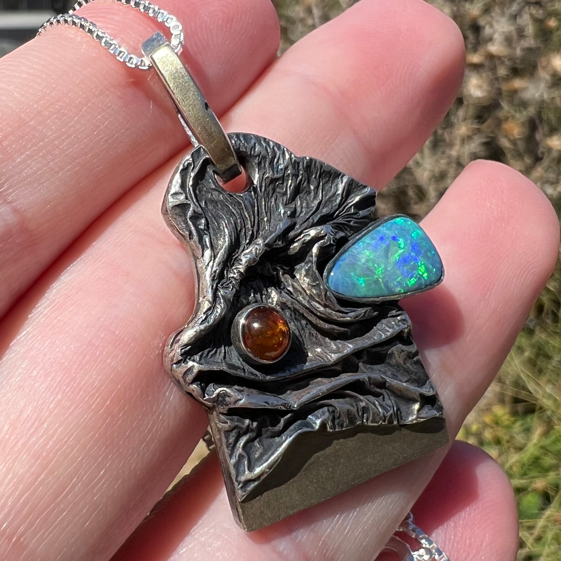 Angled close-up of a men's amber and opal doublet pendant handmade from sterling silver, held under natural light.