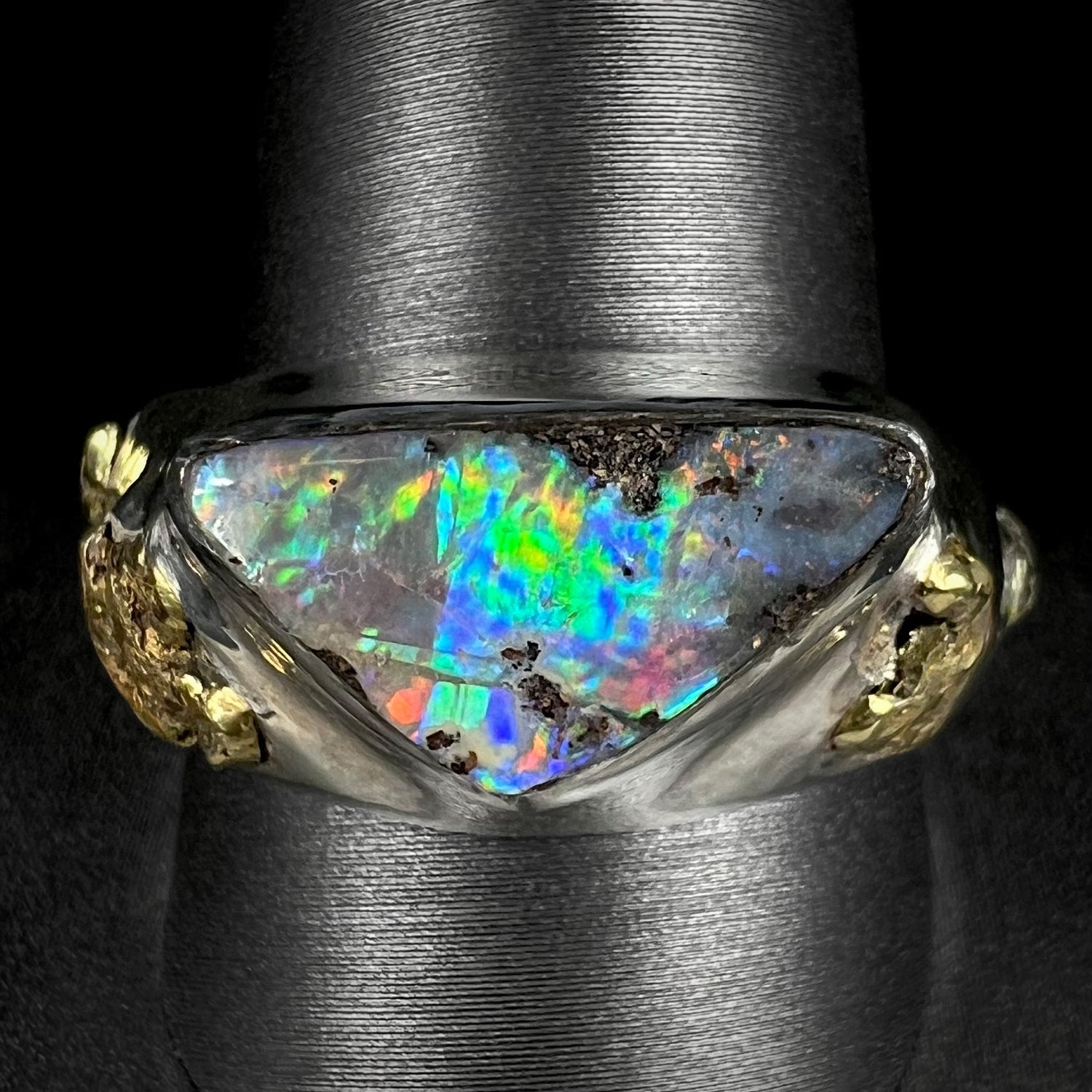 A men's Australian boulder opal ring in sterling silver with gold nugget accents shown close-up from the front on a ring display.