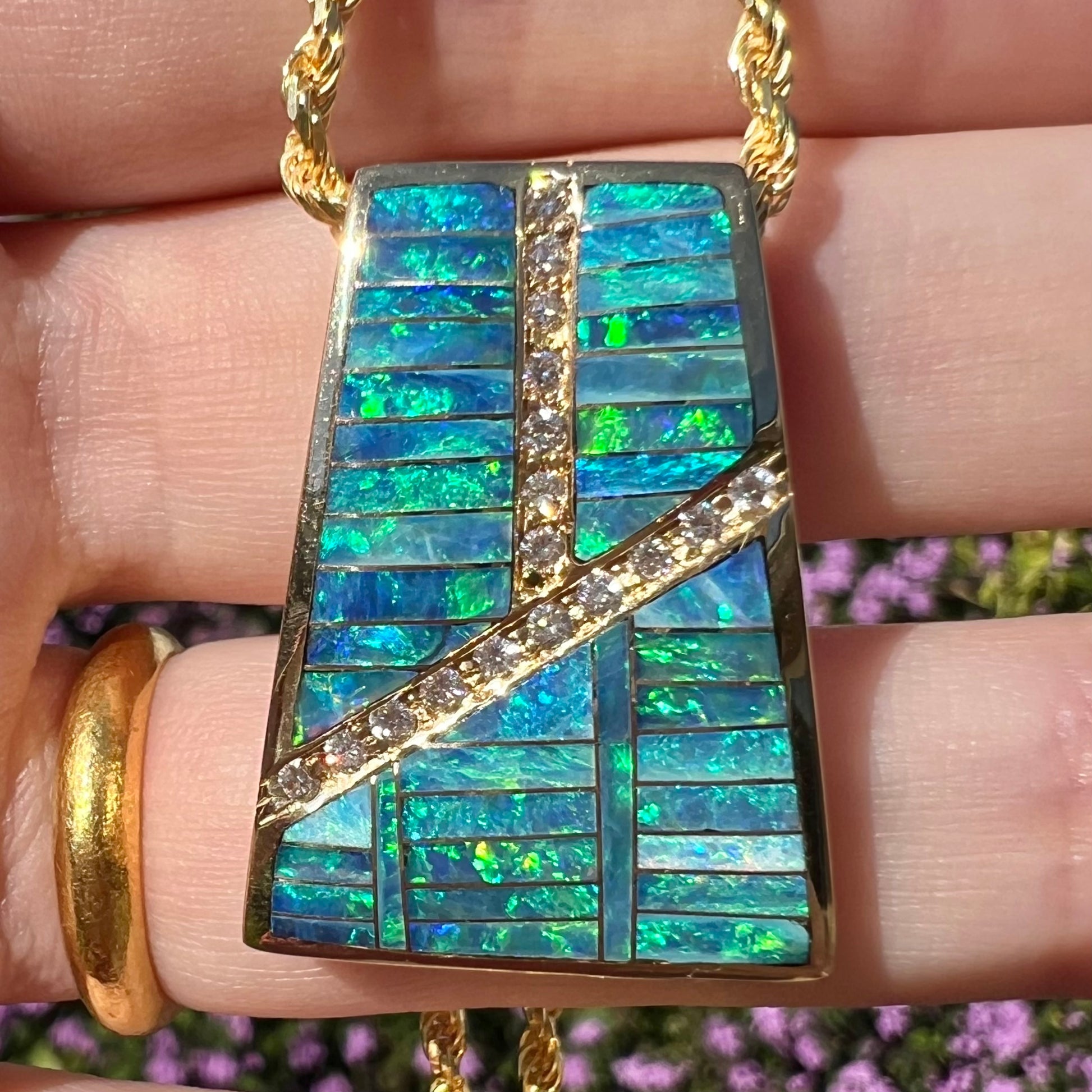 Close-up front view of a men's Australian opal inlay pendant with diamond accents in the sunlight.  The opals shine with blue and green play of color.