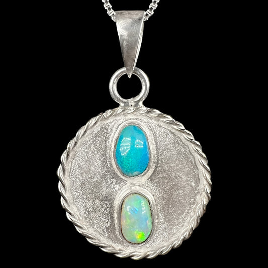 A men's sterling silver two-stone Australian opal medallion pendant with a round, textured rope design, shown close-up on a black background.