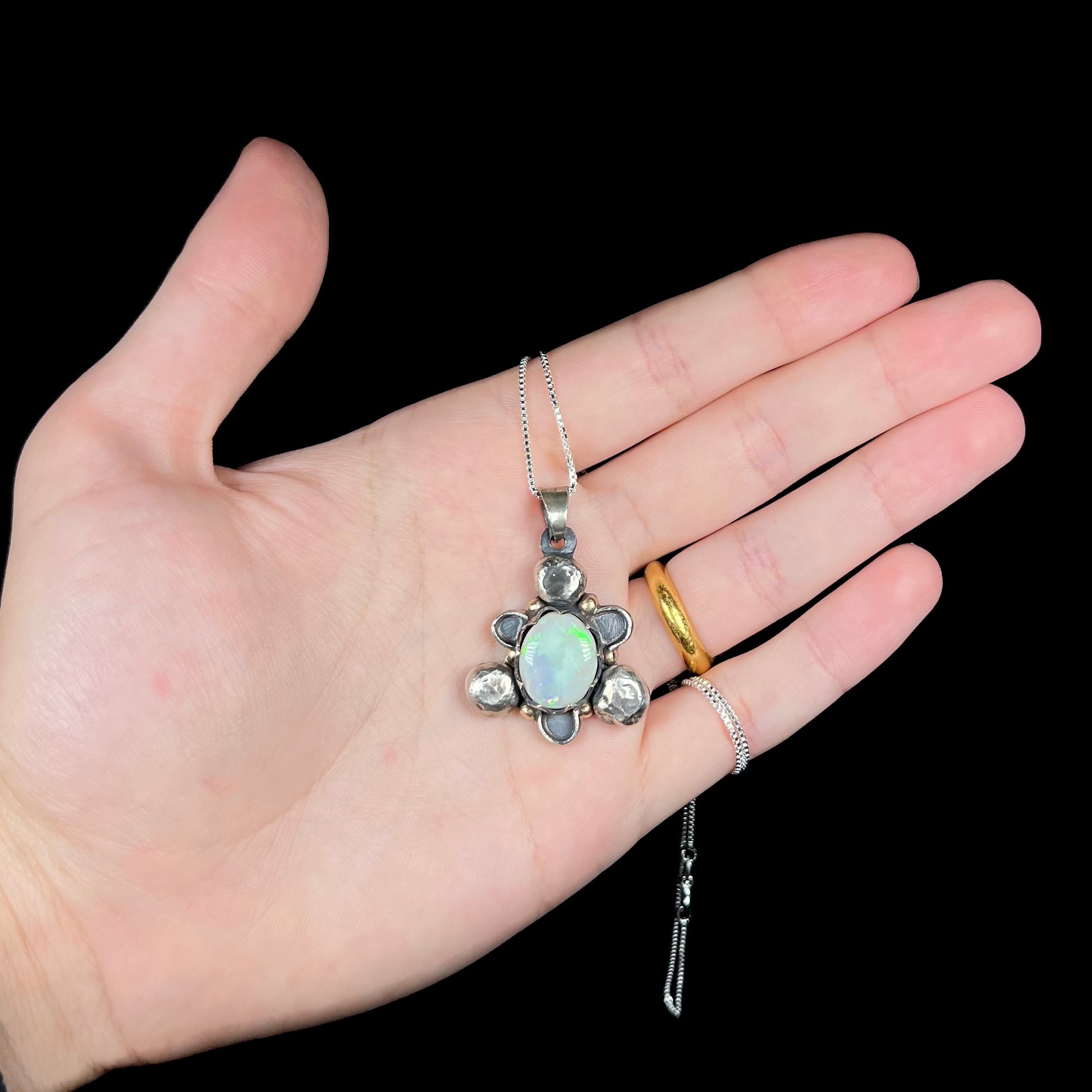 A men's rustic two-tone sterling silver and gold Australian opal pendant, held in a hand against a black backdrop.