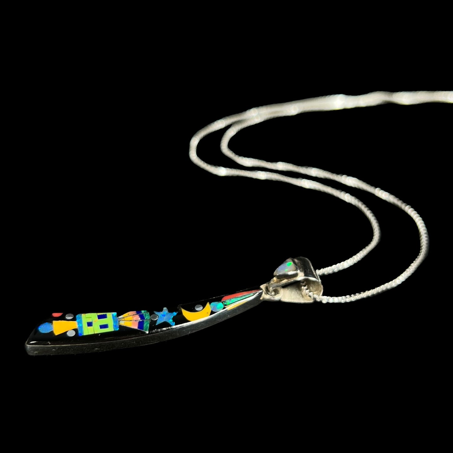 A men's sterling silver black onyx and opal inlay necklace with a Southwest-inspired motif shown from angle laying on black background.