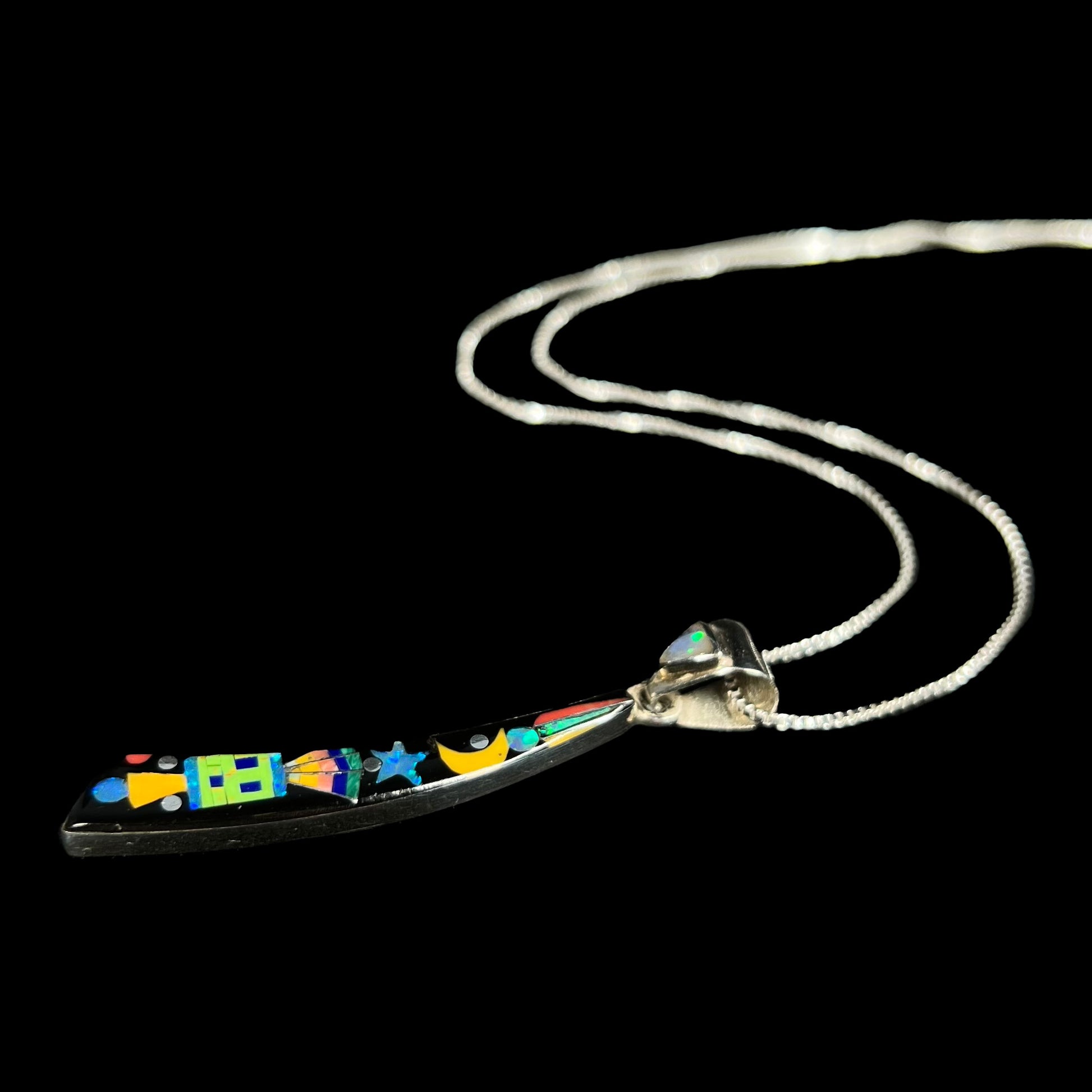 A men's sterling silver black onyx and opal inlay necklace with a Southwest-inspired motif shown from angle laying on black background.
