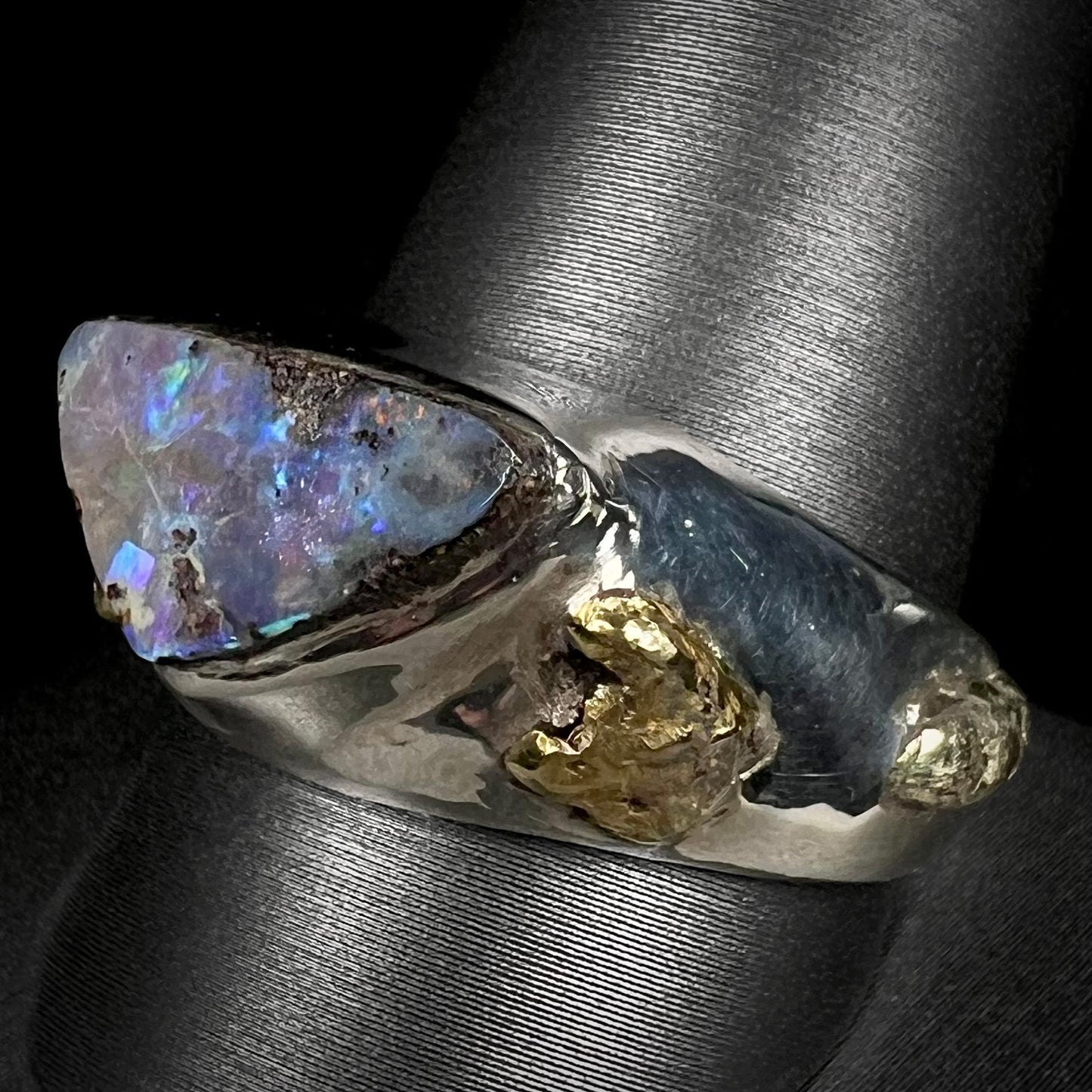 Angled view of a men's boulder opal and 21k gold nugget ring shown on a ring display.  The opal appears a cool blue color with little fire.