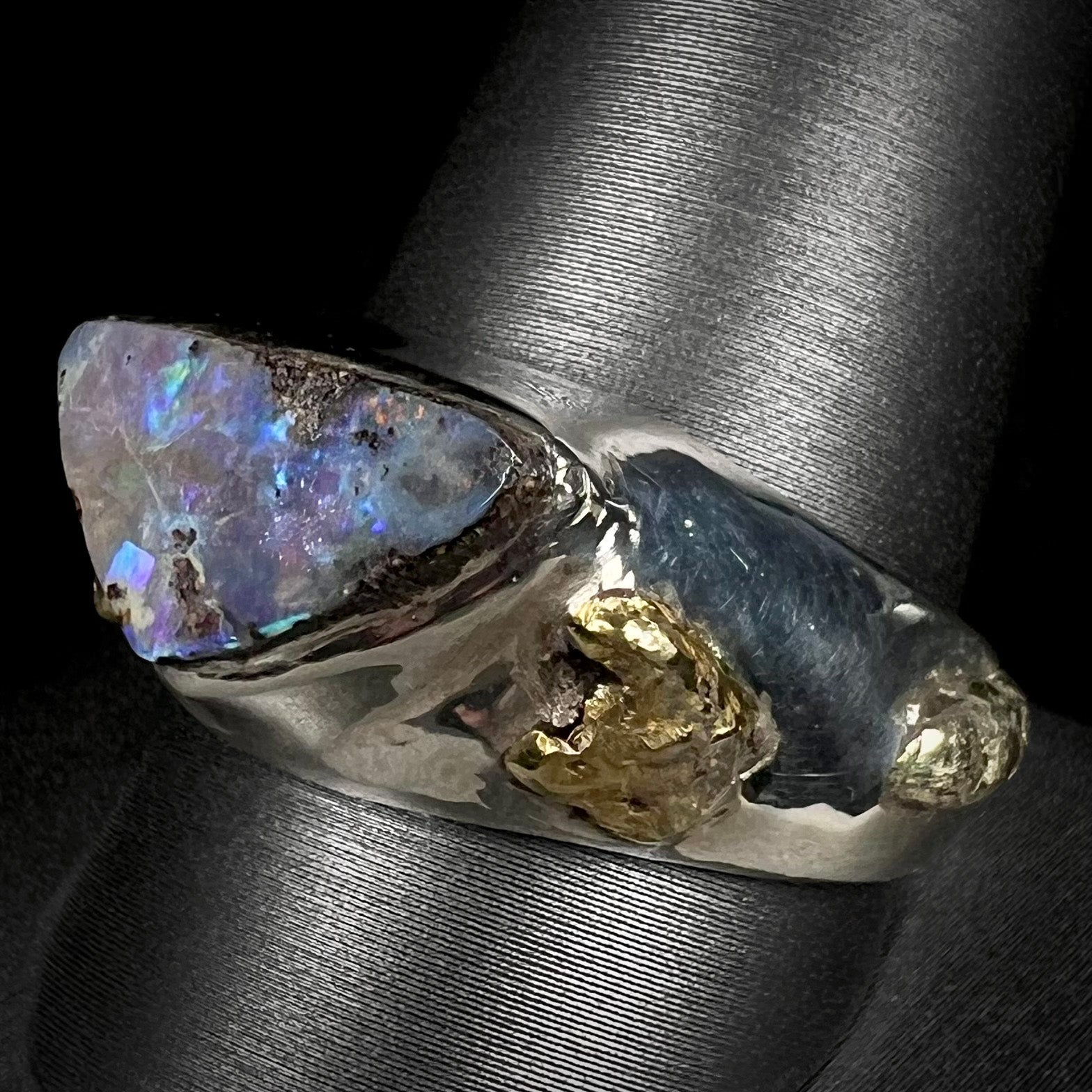 Angled view of a men's boulder opal and 21k gold nugget ring shown on a ring display.  The opal appears a cool blue color with little fire.
