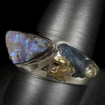 Angled view of a men's boulder opal and 21k gold nugget ring shown on a ring display.  The opal appears a cool blue color with little fire.