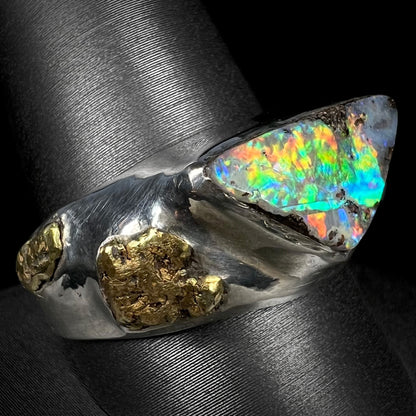 Vibrant multicolor fire plays from a men's boulder opal and gold nugget ring made from sterling silver as it is shown at an angle on a ring display.