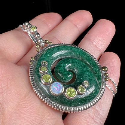 A men's aventurine koru necklace, accented with opal and peridot, shown in a hand close-up from an angle.