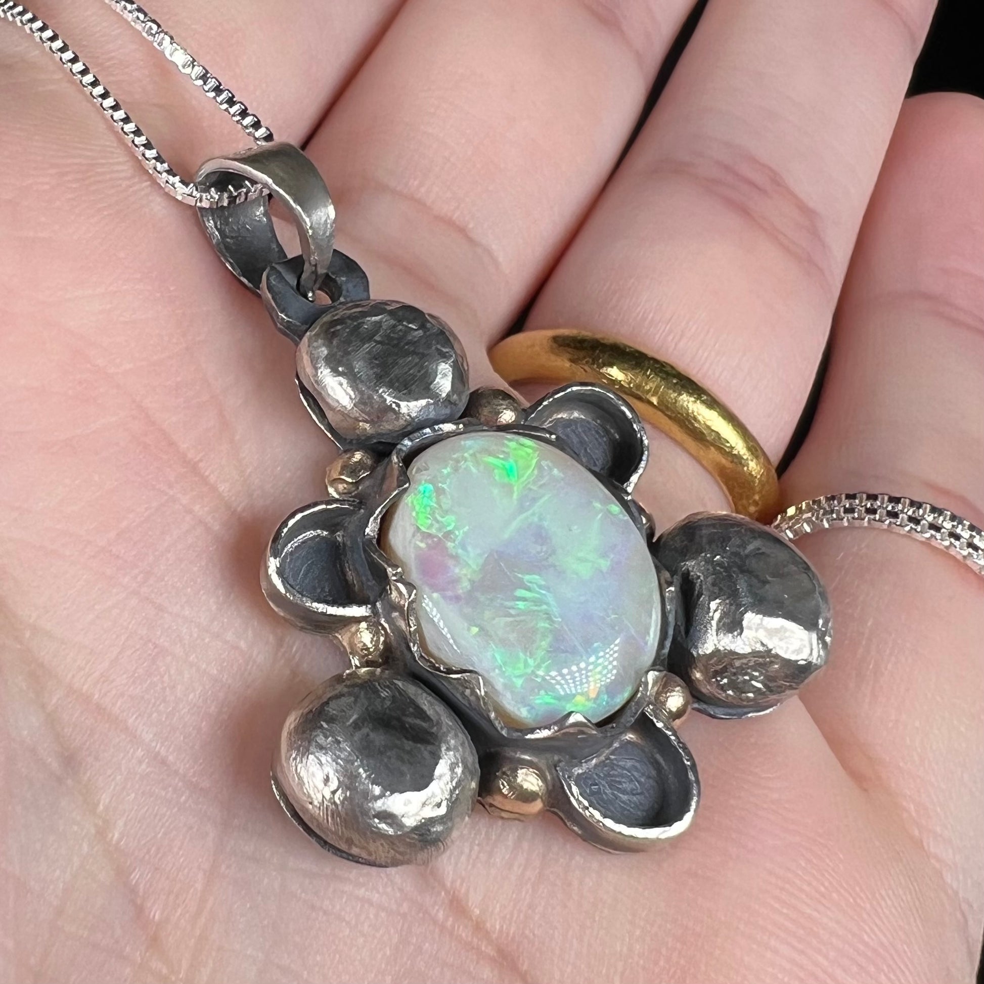 Angled close-up of a men's rustic two-tone sterling silver and gold Australian opal pendant, held in a hand.