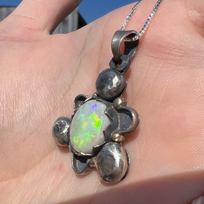 Angled close-up sunlit view of a two-tone silver and gold men's opal pendant with green flashes.