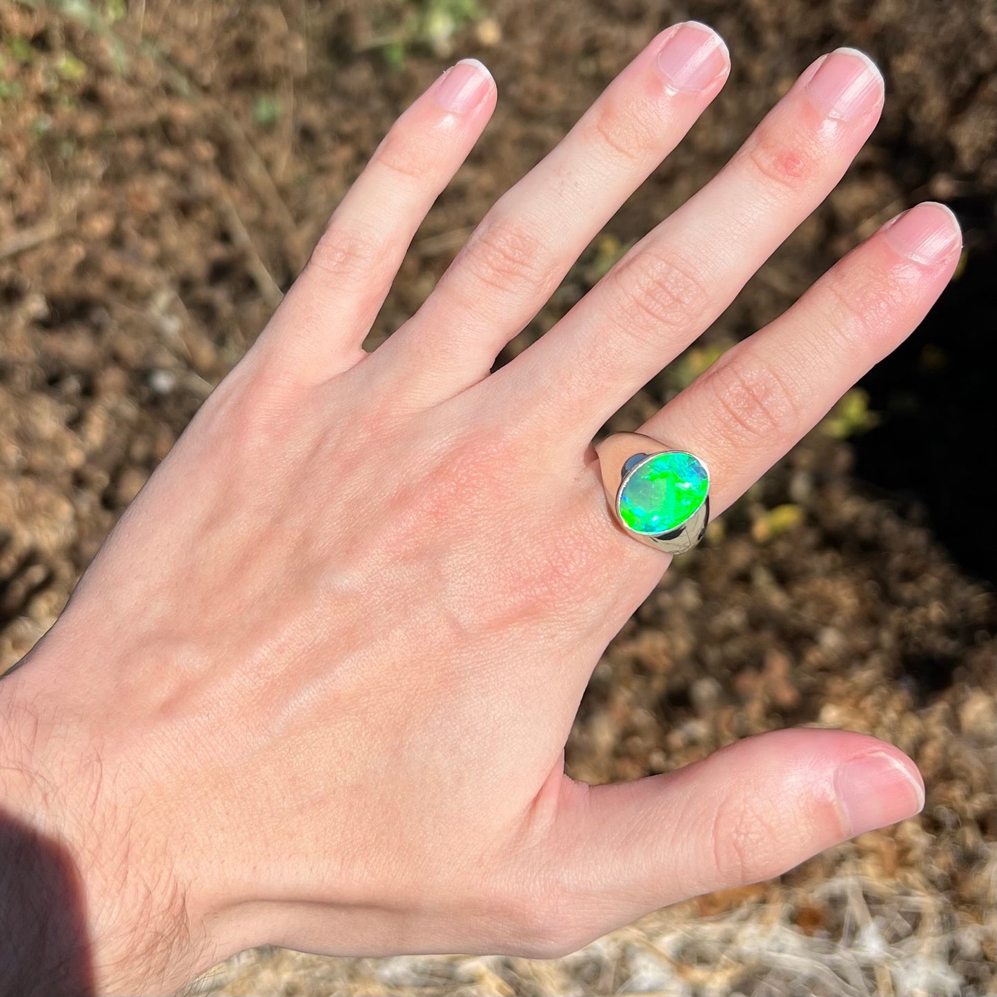 Hand wearing green crystal opal men's ring in sunlight