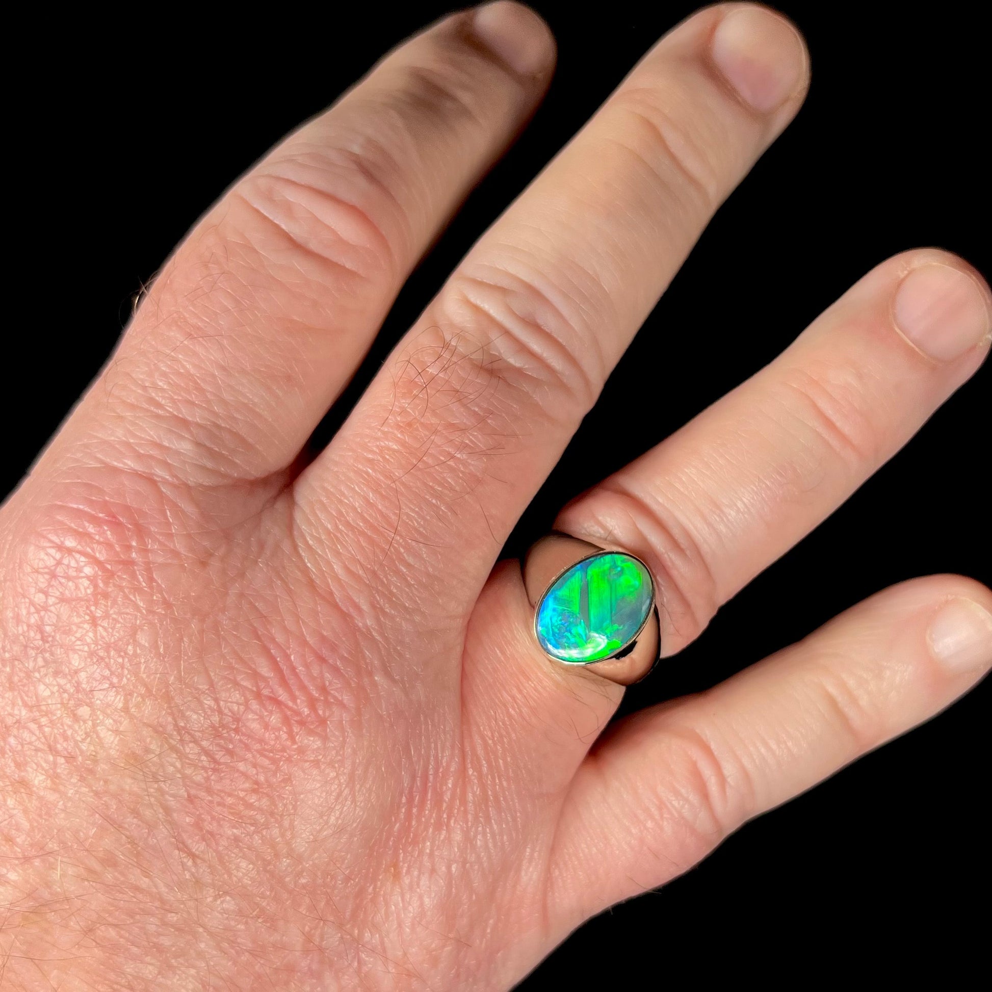 Man's hand wearing a green Australian crystal opal men's ring in white gold