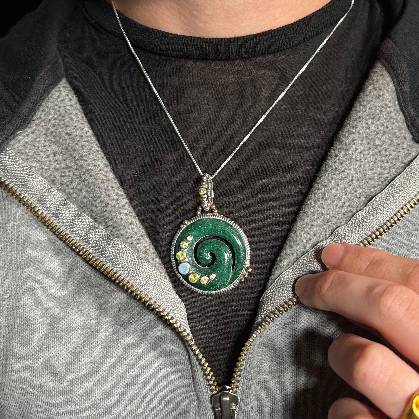 A men's aventurine koru spiral necklace with peridot and opal accents, worn around a neck against a dark shirt.