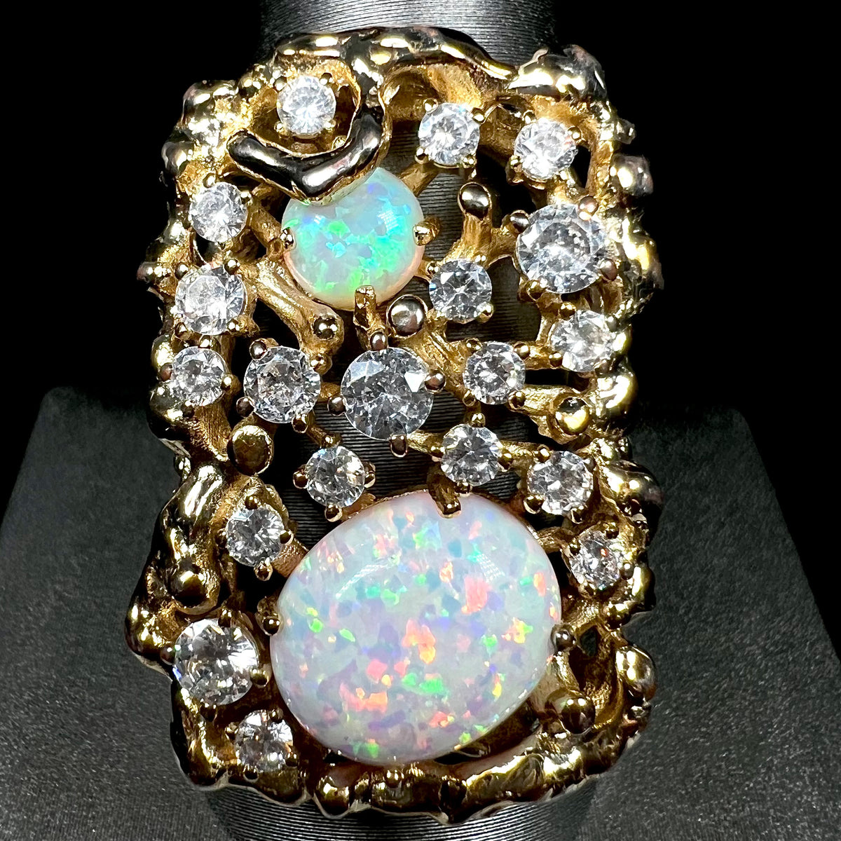 Close-up of large, gold-tone men's statement ring set with two lab-created opals and round cubic zirconia stones of different sizes.