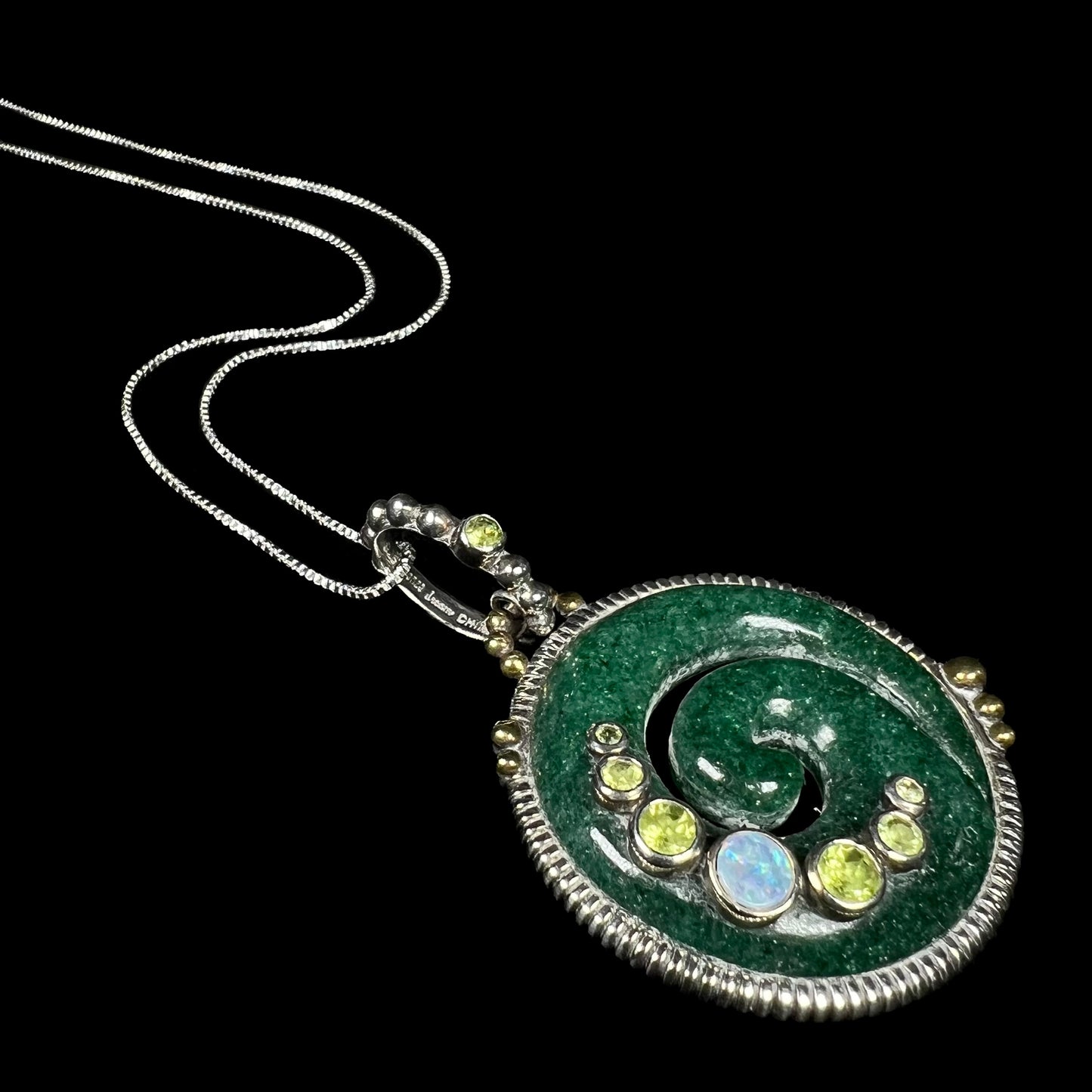 A men's green aventurine koru necklace set with opal and aventurine accents, laying at an angle on black background.