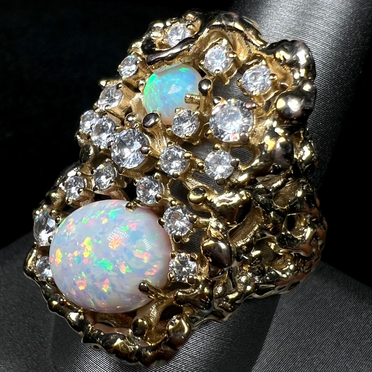 Angled close-up of 1970s brutalist style men's bird's nest ring set with lab-created opals and CZ stones, shown on ring display.